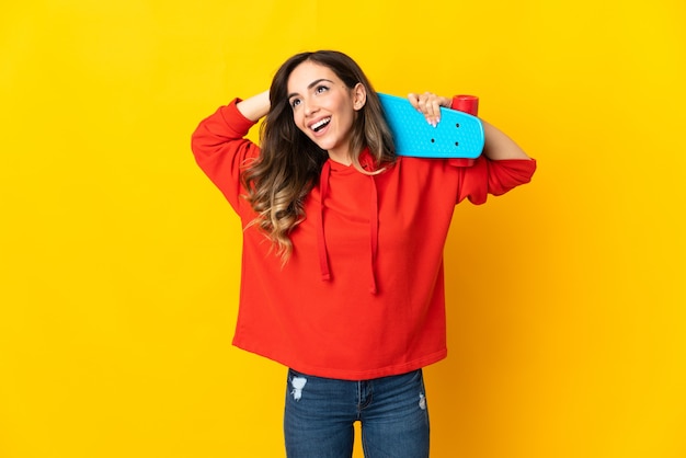 Young caucasian woman isolated on yellow wall with a skate and looking up