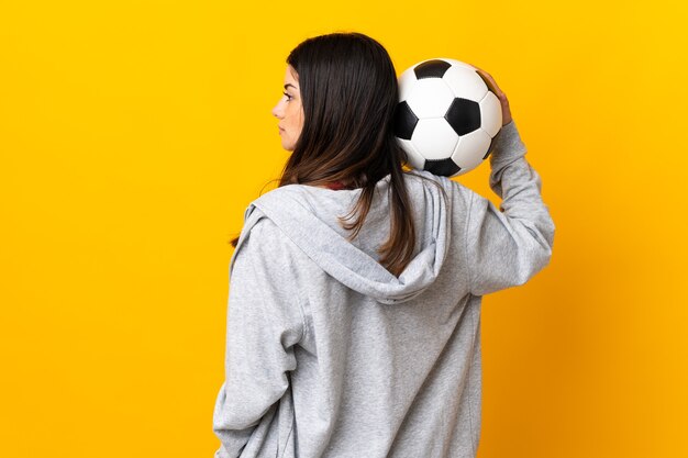 Giovane donna caucasica isolata sulla parete gialla con pallone da calcio