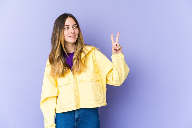 Young caucasian woman joyful and carefree showing a peace symbol with fingers.