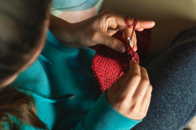 Young Caucasian woman knitting a scarf with red yarn Sitting on the sofa in the living room