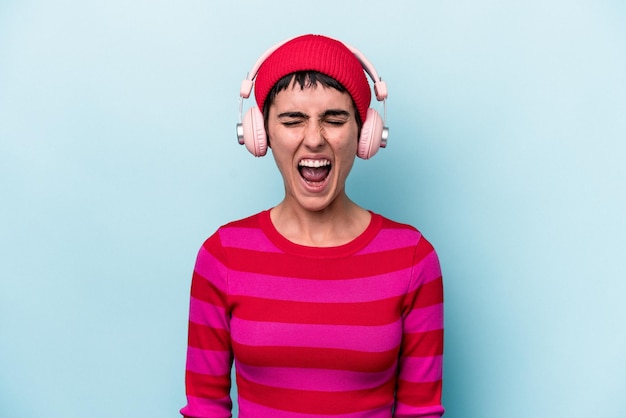 Young caucasian woman listening to music isolated on background screaming very angry and aggressive.