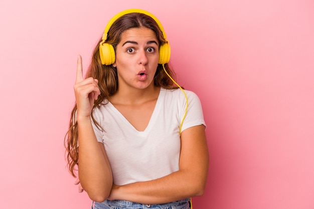 Young caucasian woman listening to music isolated on pink background  having some great idea, concept of creativity.