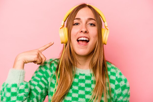 Young caucasian woman listening to music isolated on pink background