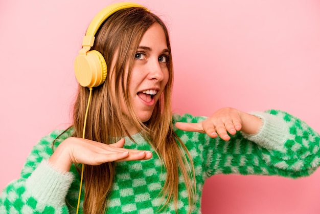 Young caucasian woman listening to music isolated on pink background