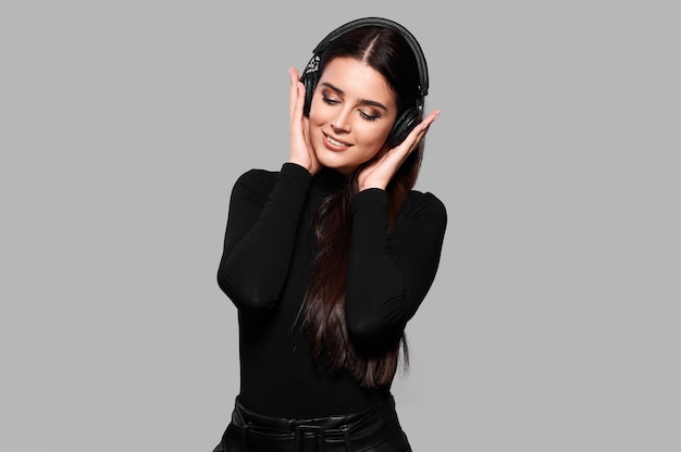 Young caucasian woman listening music in wireless headhones on isolated background