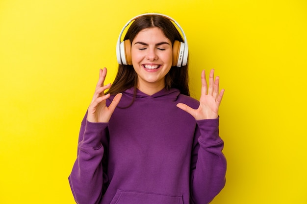 Young caucasian woman listening to music with headphones isolated on pink wall joyful laughing a lot. Happiness concept.