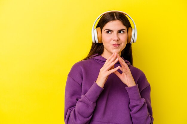 Giovane donna caucasica che ascolta la musica con le cuffie sul rosa che compongono il piano in mente, creando un'idea.