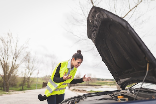 Foto giovane donna caucasica guardando il motore dell'auto, non sa cosa fare, auto guasta in mezzo alla strada. concetto di assistenza stradale e dell'automobile.