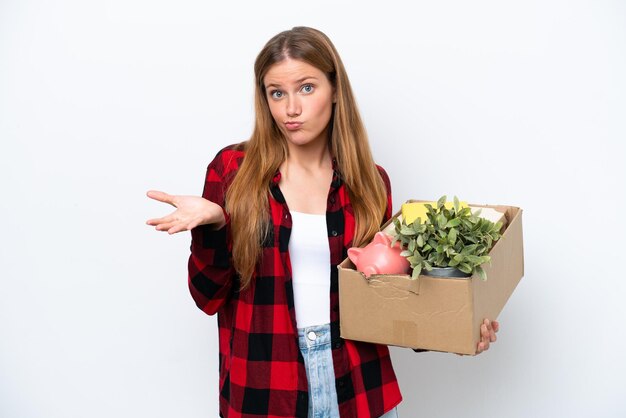 手を上げながら疑問を持つ白い背景で隔離のものでいっぱいの箱を拾いながら動きを作る若い白人女性