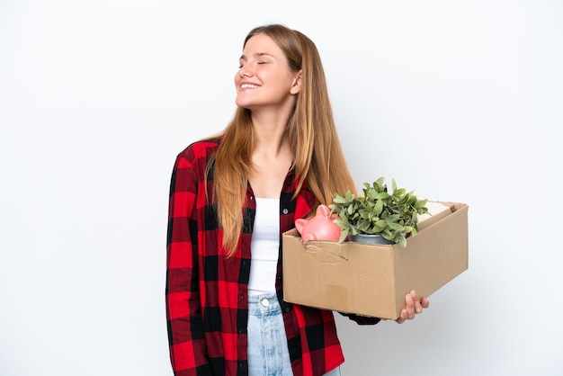 Young caucasian woman making a move while picking up a box full of things isolated on white background laughing