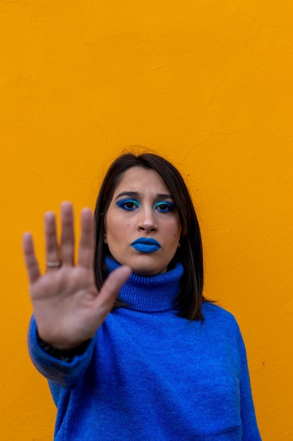 Young caucasian woman making stop sign with hand saying no looking at camera vertical Yellow studio background