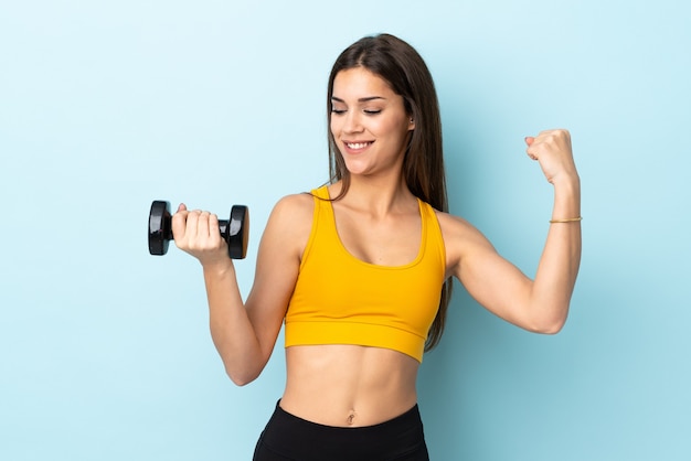 Young caucasian woman making weightlifting on blue celebrating a victory