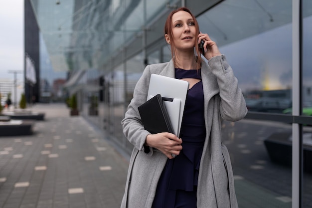 Young caucasian woman manager speaks on the phone holding documents in her hand on the background of