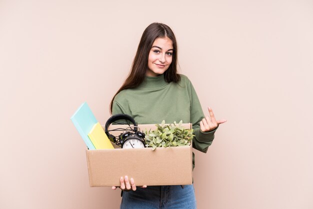 Young caucasian woman moving to a new home pointing with finger at you as if inviting come closer.