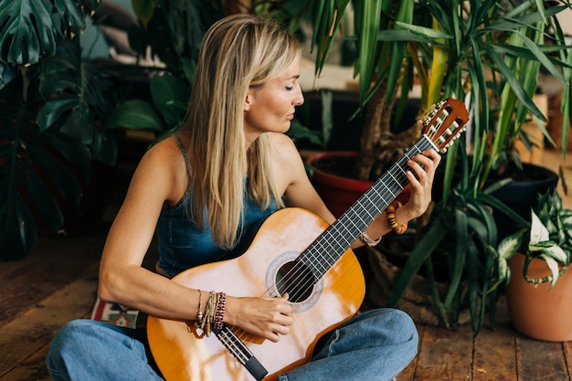 young caucasian woman musician sitting on floor in home greenhouse playing guitar