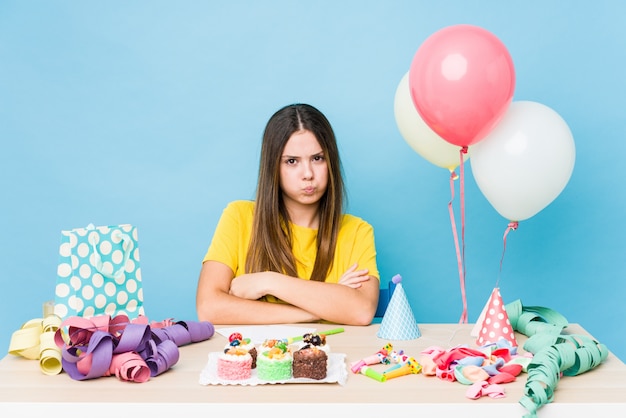 Young caucasian woman organizing a birthday blows cheeks, has tired expression