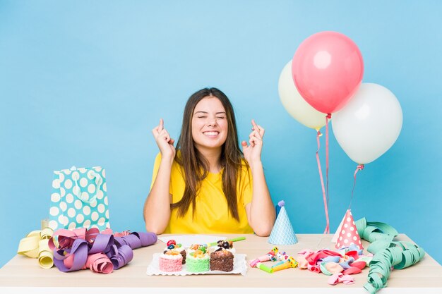 Young caucasian woman organizing a birthday crossing fingers for having luck