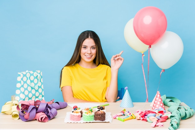 Giovane donna caucasica che organizza un compleanno che sorride allegramente indicando con l'indice via.