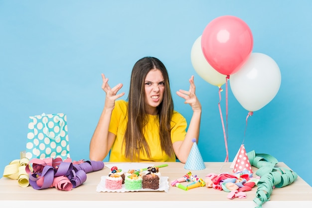 Young caucasian woman organizing a birthday upset screaming with tense hands.