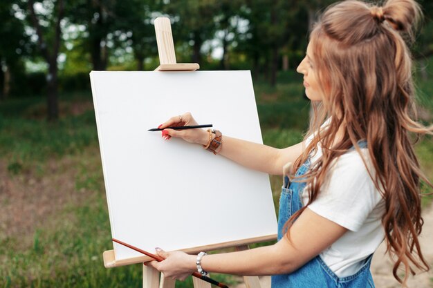 Young caucasian woman painting on canvas outside