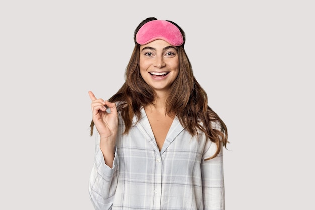 Photo young caucasian woman in pajamas with mask pointing to the side