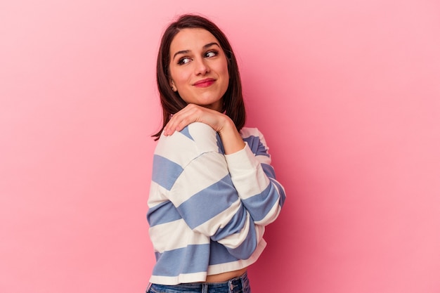 Young caucasian woman on pink background hugs, smiling carefree and happy.