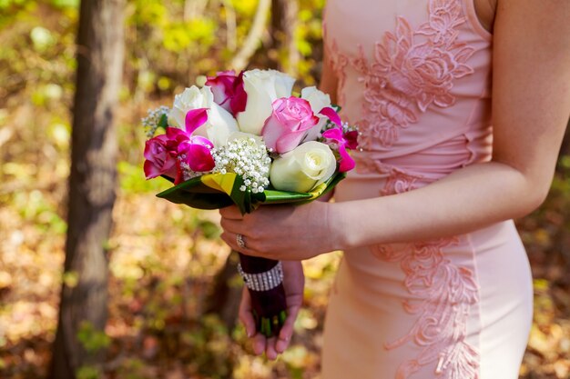 Young caucasian woman in pink lace dress holds a bouquet with flowers and pink garden roses in her hands