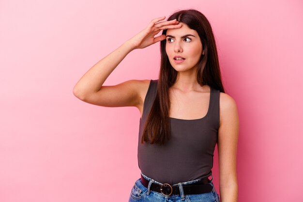 young caucasian woman on pink looking far away keeping hand on forehead.