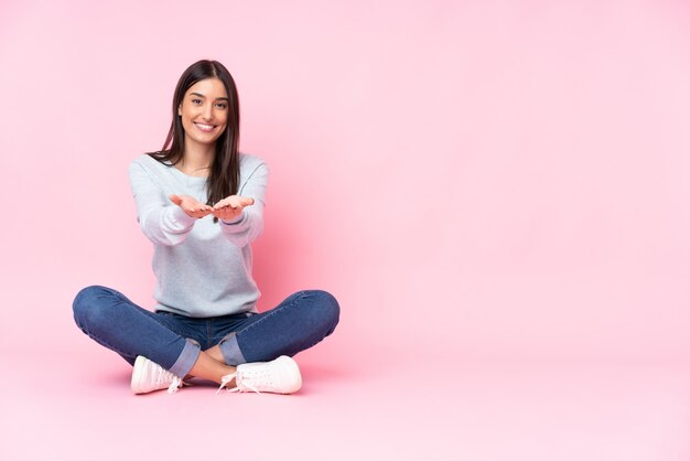 Young caucasian woman on pink wall holding blank space on the palm