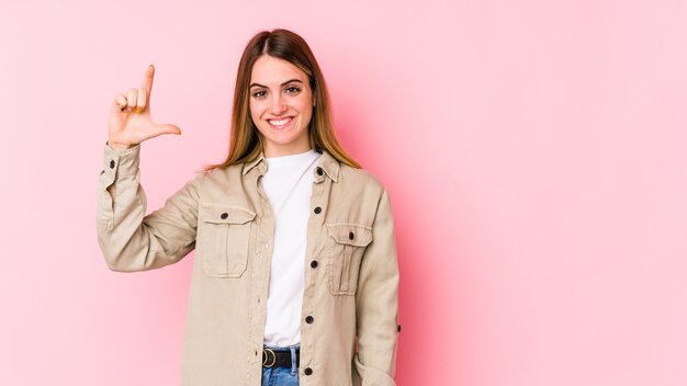 Young caucasian woman on pink wall holding something little with forefingers