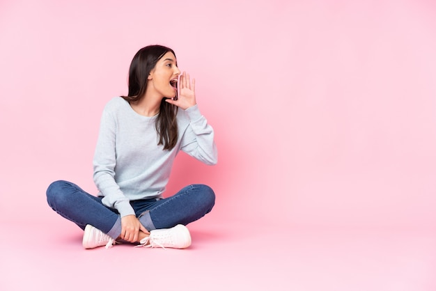 Young caucasian woman on pink wall shouting with mouth wide open to the lateral