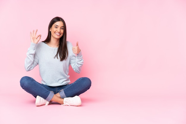 Young caucasian woman on pink wall showing ok sign and thumb up gesture