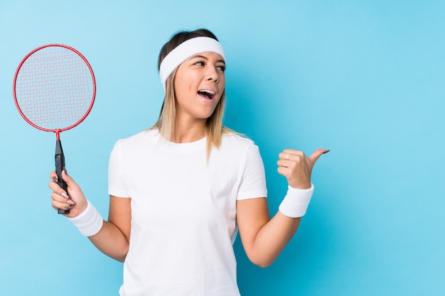 Young caucasian woman playing badminton points with thumb finger away, laughing and carefree.