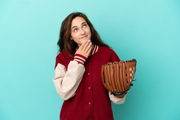 Young caucasian woman playing baseball isolated on blue background looking up while smiling