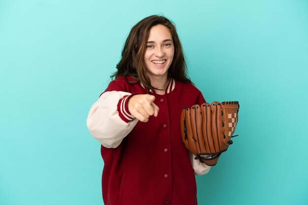 Young caucasian woman playing baseball isolated on blue background surprised and pointing front