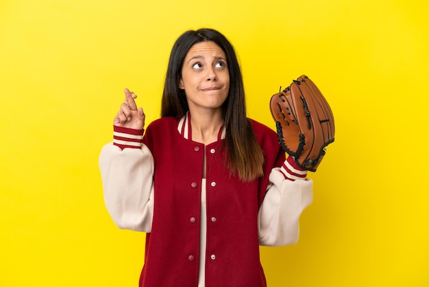 Young caucasian woman playing baseball isolated on yellow background with fingers crossing and wishing the best