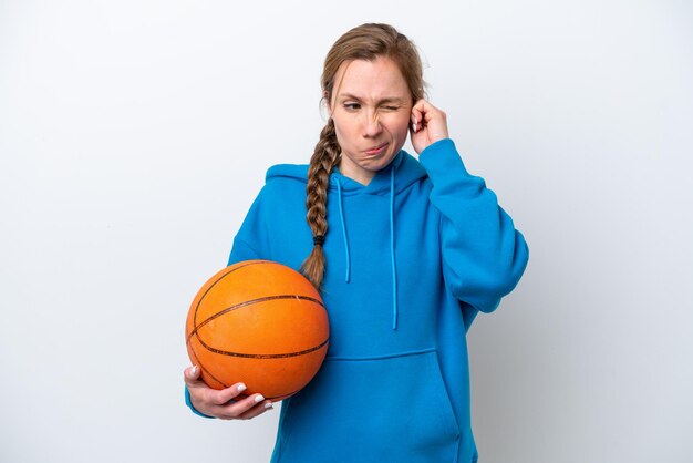 Young caucasian woman playing basketball isolated on white\
background frustrated and covering ears