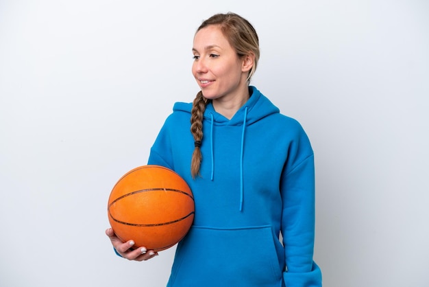 横を見て笑っている白い背景で隔離のバスケットボールをしている若い白人女性