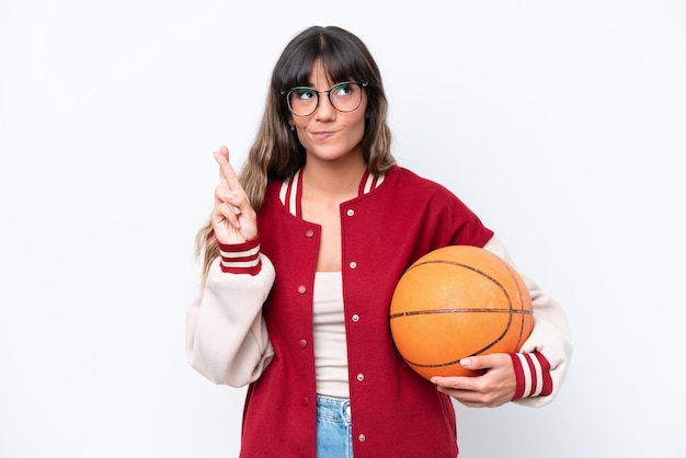 Young caucasian woman playing basketball isolated on white background with fingers crossing and wishing the best