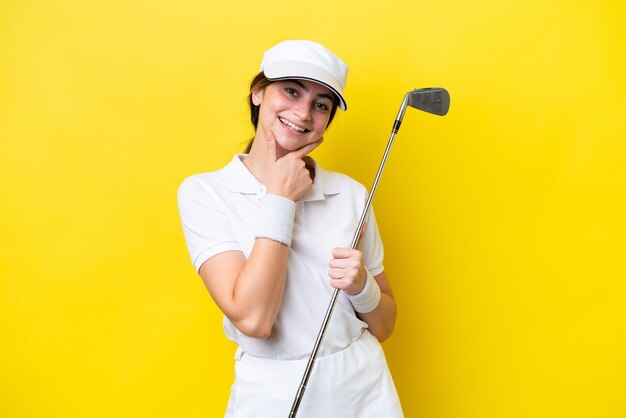 Young caucasian woman playing golf isolated on yellow background happy and smiling