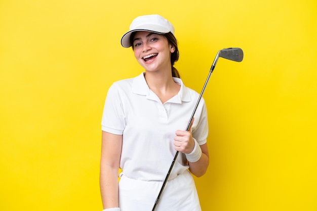 Молодая кавказская женщина, играющая в гольф на желтом фоне, смеется