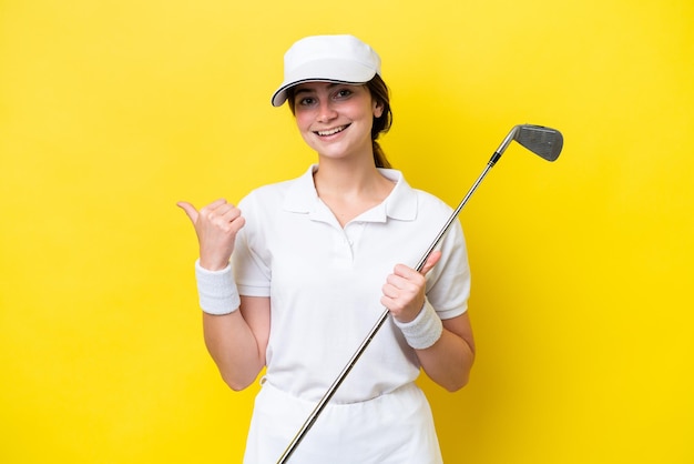 Young caucasian woman playing golf isolated on yellow background pointing to the side to present a product