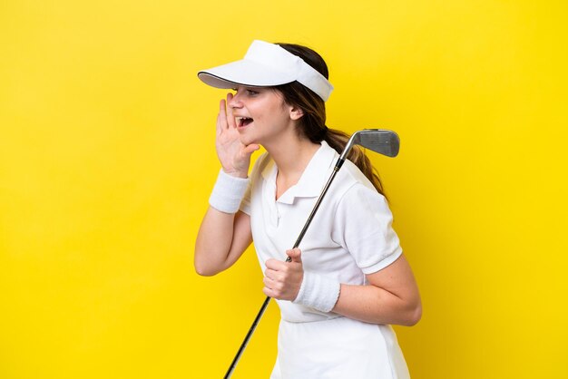 Young caucasian woman playing golf isolated on yellow background shouting with mouth wide open to the side