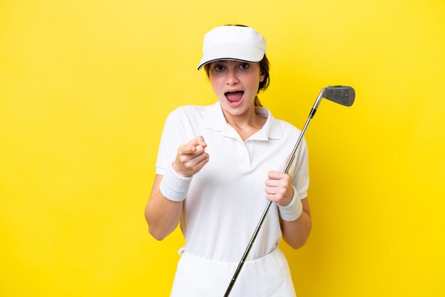 Young caucasian woman playing golf isolated on yellow background surprised and pointing front