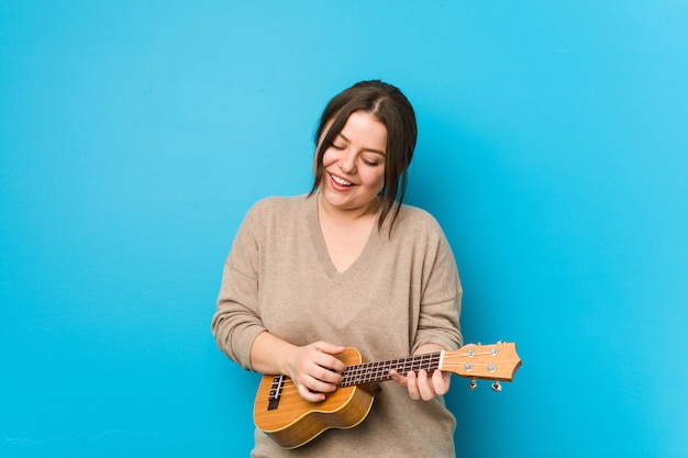 Giovane donna caucasica che gioca ukelele su una parete blu