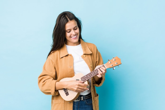 Young caucasian woman playing ukelele isolated on a blue wall