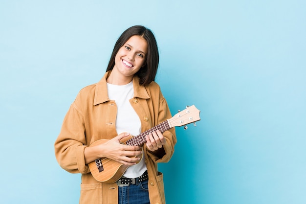 Young caucasian woman playing ukelele isolated on a blue