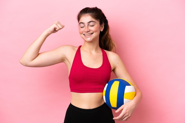 Young caucasian woman playing volleyball isolated on pink background doing strong gesture