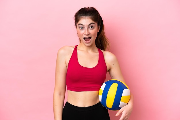 Young caucasian woman playing volleyball isolated on pink
background with surprise facial expression