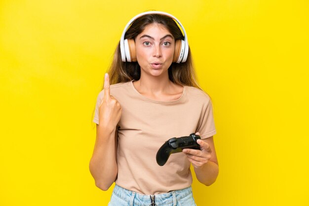 Young caucasian woman playing with a video game controller isolated on yellow background intending to realizes the solution while lifting a finger up